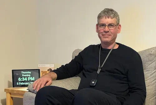 A man sitting in a comfy chair surrounded by assistive technology to support his independence