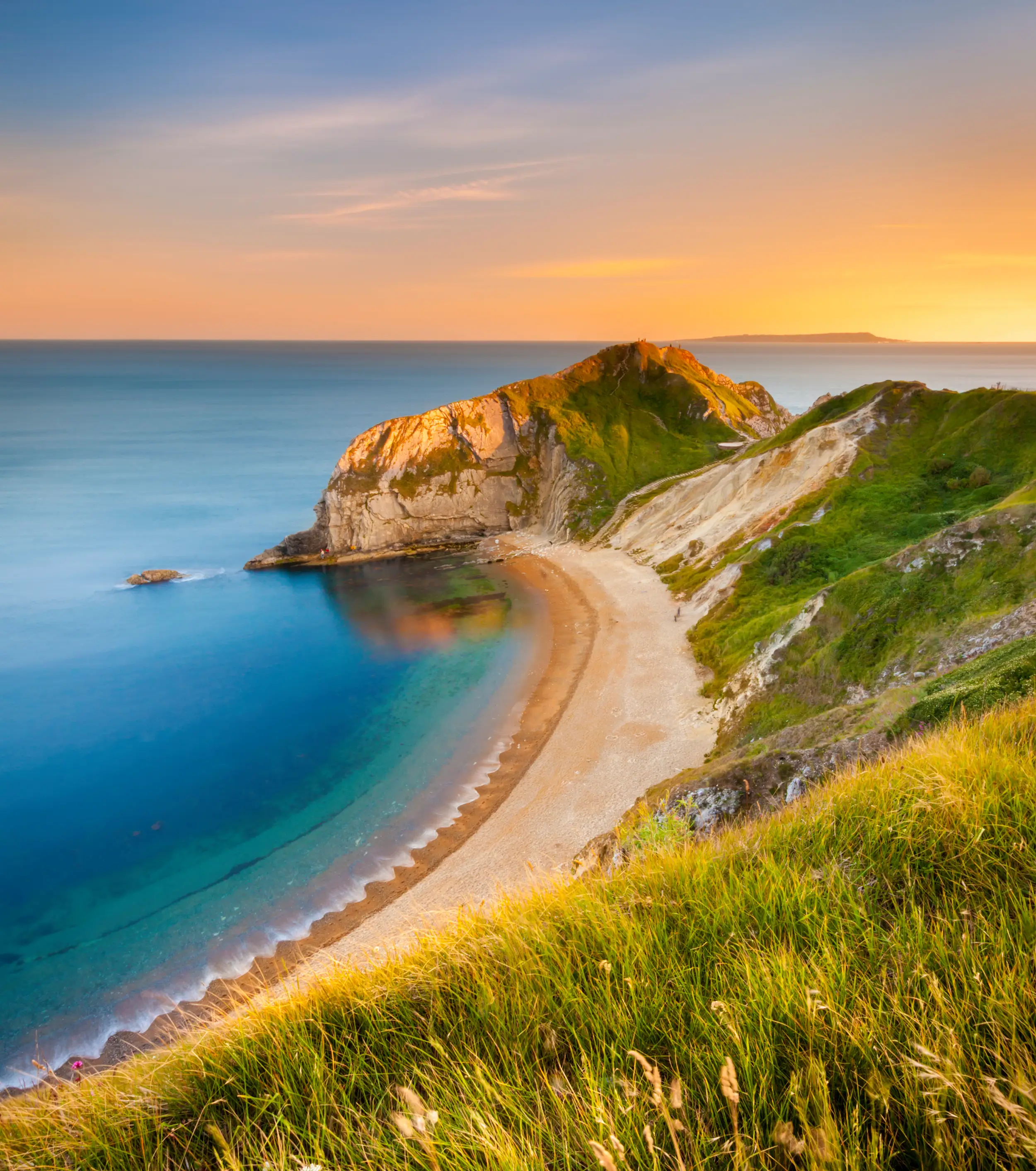 A Dorset cliff edge with a sandy shore, deep blue sea and sunset