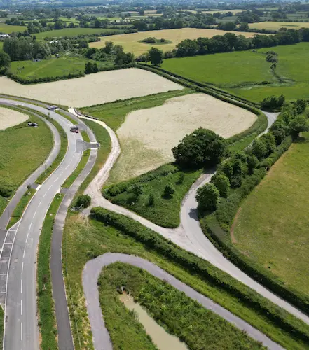 Aerial view of a rural road and shared-use path winding through fields and countryside, bordered by hedgerows and trees.