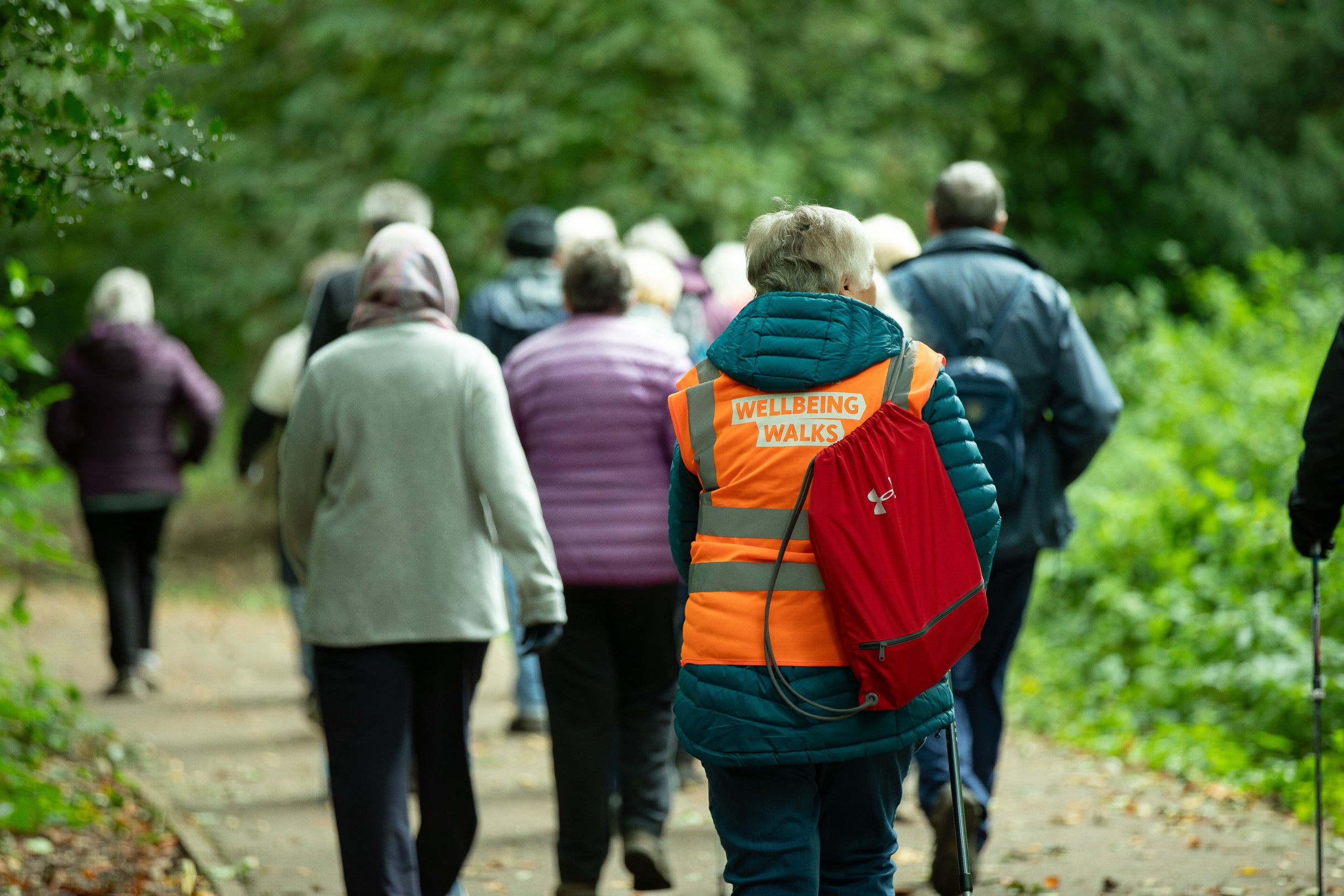 Group of people walking along a path with greenery, wearing coats