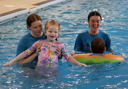 Children and instructors taking part in a supported swimming session in an indoor.