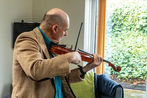 A man playing a violin in front of a window