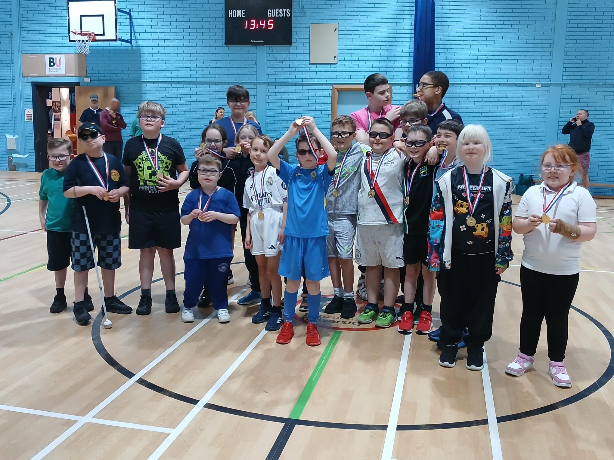 A group of young children with medals around their necks standing in a sports hall.