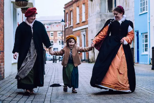 People in historical costume walking with a child along a town street.