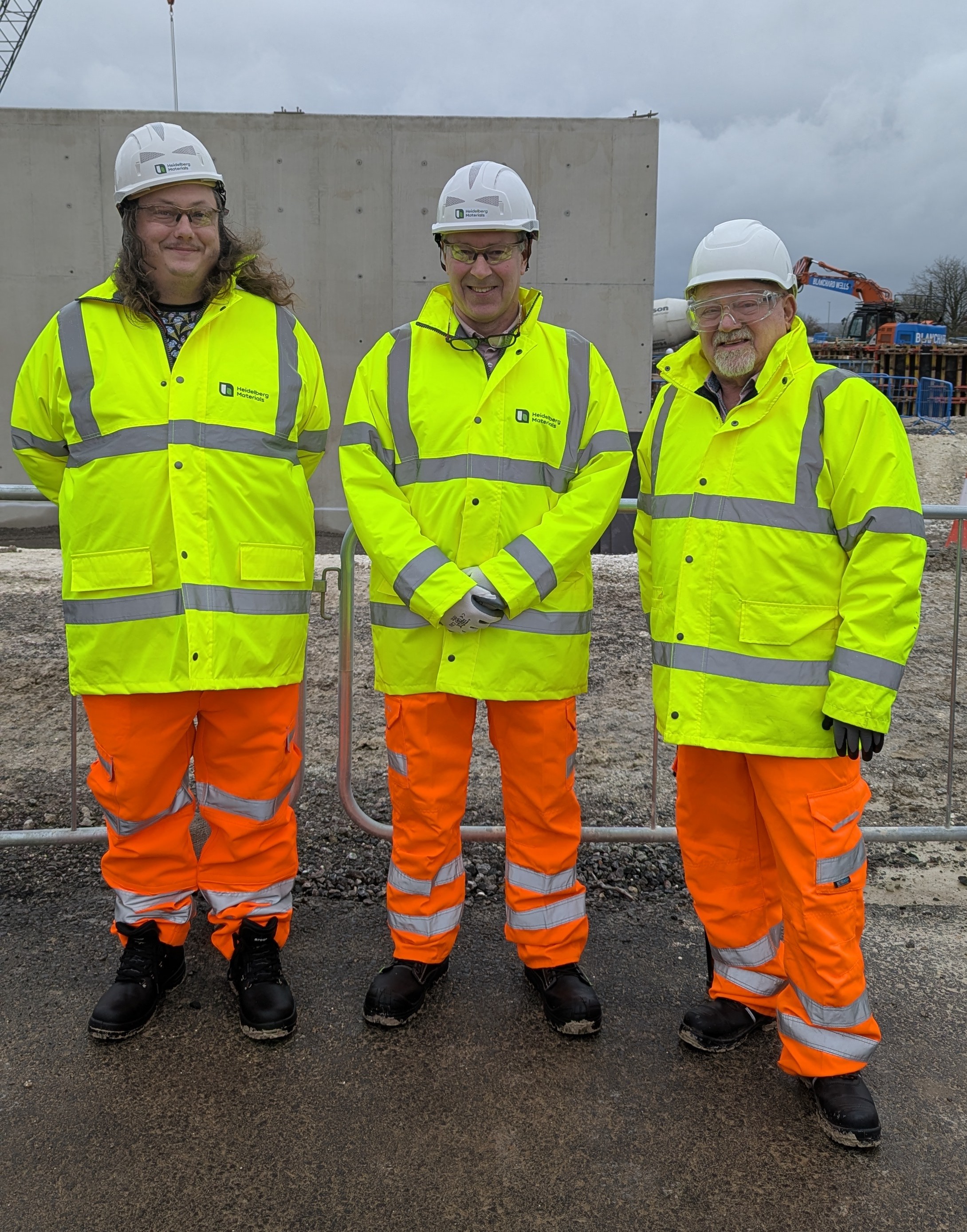3 construction workers wearing hi vis jackets and white hard hates on a building site