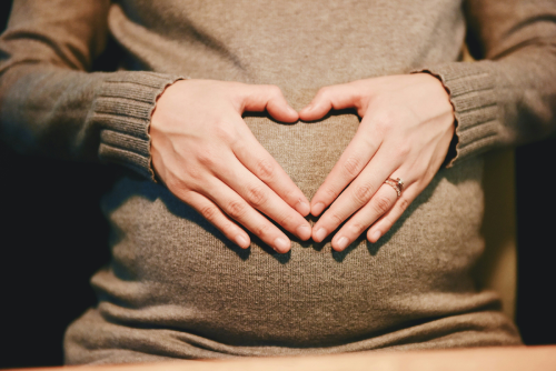 Mother pradling bump with her hands making a heart symbol