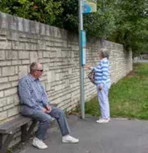 A couple waiting at a bus stop in the village of Abbotsbury, with seating provided. The image highlights investment in rural transport infrastructure to enhance accessibility and encourage public transport use.