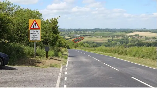 Viewpoint 14: View looking north from the road near the top of Spread Eagle Hill The northern and central parts of the woodland within the site boundary are visible (outlined in red) in the middle distance.The density and mass of the woodland will be reduced within the view as a result of the proposals.