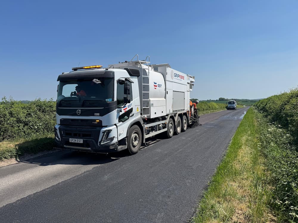 A white lorry resurfacing the road under a blue sky.