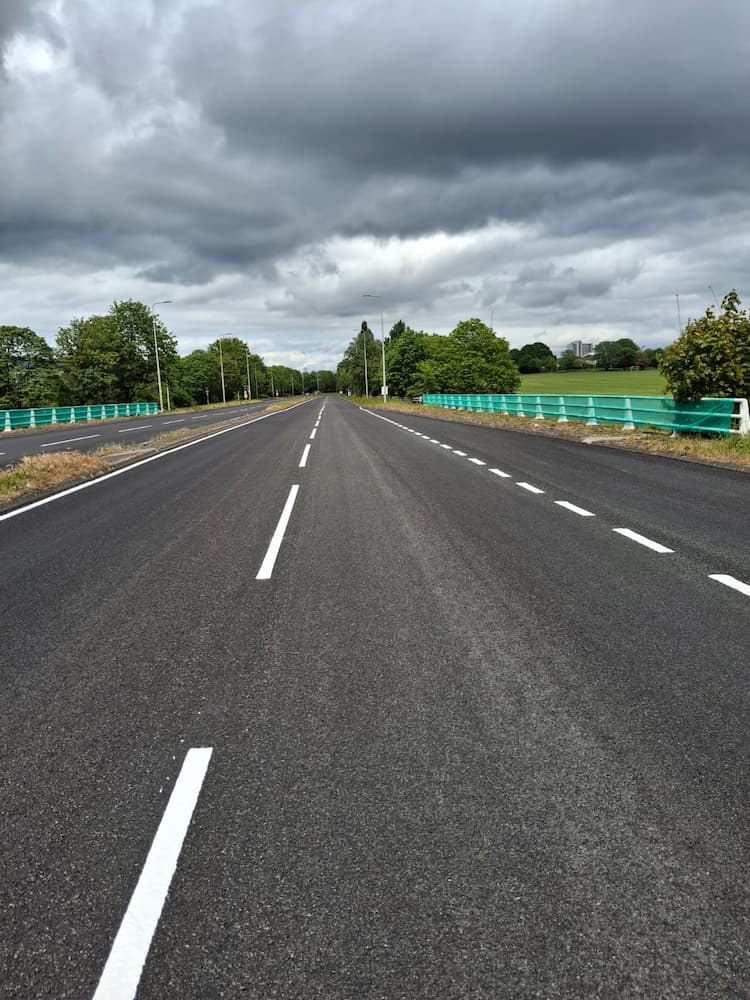 A brand new resurfaced road with white markings under a cloudy sky.
