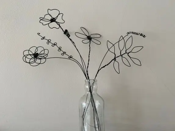A clear vase with black flowers carved from wire with a beige background