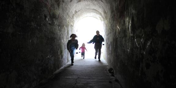 an adult and two children run through a dark tunnel