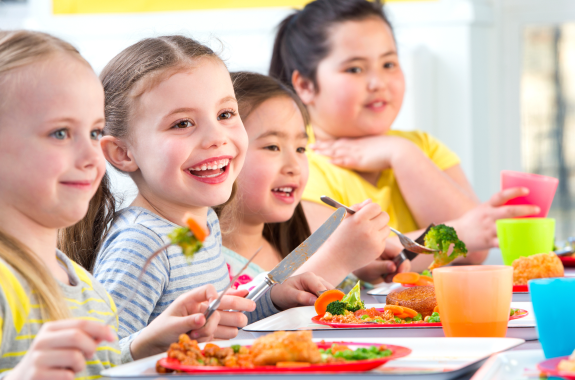 A row of school children eating food from colourful plates