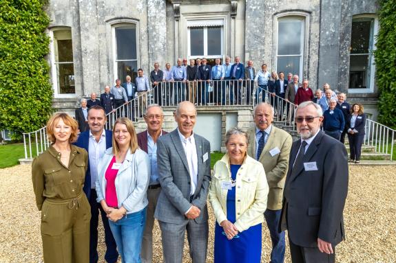 A group of men and women standing in front of a stately manor house