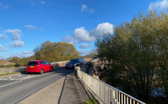 A red car approaching a bridge meets a black car coming towards it
