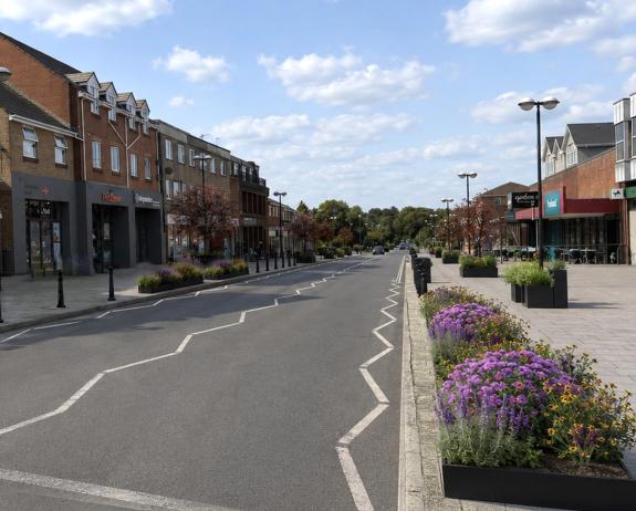 An artist impression of a high street with planters containing purple and yellow flowers along the edge of the road