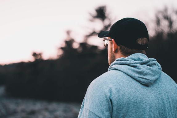 A stock image of a man looking into the distance, he is wearing a hat and glasses and a grey top