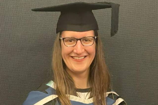 A woman with brown hair and glasses, wearing a graduation gown and cap.